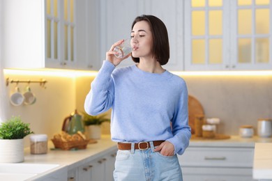 Photo of Young woman drinking water from in kitchen