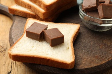 Photo of Tasty chocolate butter cubes on slice of bread on wooden table, closeup