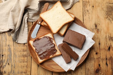 Photo of Pieces of tasty chocolate butter, slices of bread and knife on wooden table, top view