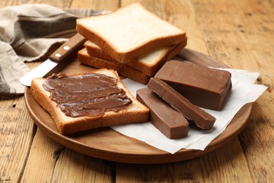 Photo of Pieces of tasty chocolate butter and slices of bread on wooden table, closeup
