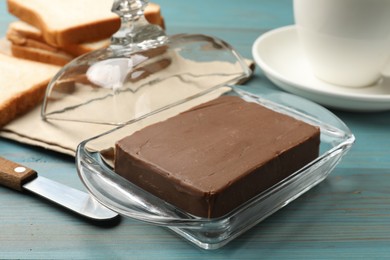 Photo of Block of tasty chocolate butter in glass keeper on light blue wooden table, closeup