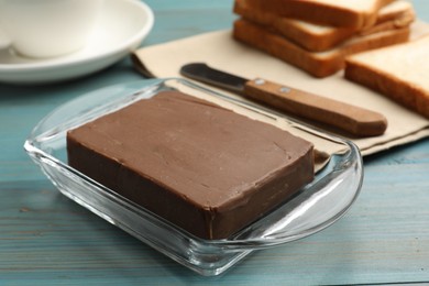 Photo of Block of tasty chocolate butter in glass keeper on light blue wooden table, closeup