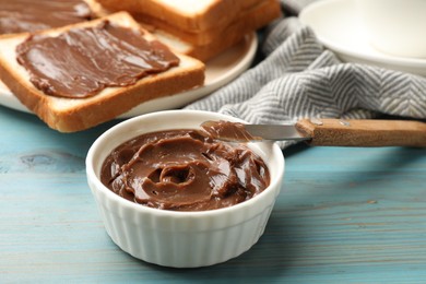 Photo of Tasty chocolate butter in bowl and knife on light blue wooden table, closeup