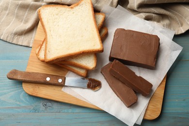 Photo of Pieces of tasty chocolate butter, slices of bread and knife on light blue wooden table, top view