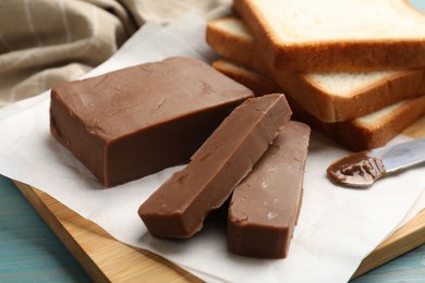 Photo of Pieces of tasty chocolate butter and slices of bread on light blue wooden table, closeup
