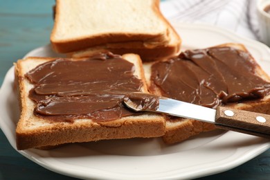 Photo of Pieces of bread with tasty chocolate butter and knife on light blue wooden table, closeup