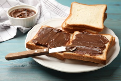 Photo of Pieces of bread with tasty chocolate butter and knife on light blue wooden table, closeup