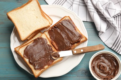 Photo of Tasty chocolate butter in bowl, slices of bread and knife on light blue wooden table, flat lay