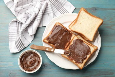 Photo of Tasty chocolate butter in bowl, slices of bread and knife on light blue wooden table, flat lay