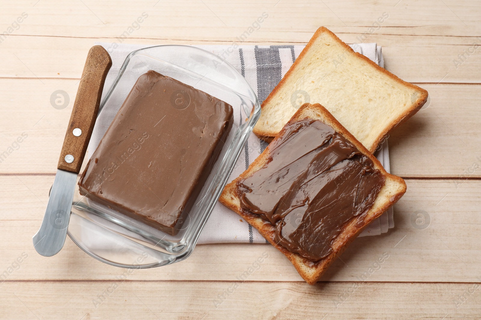 Block of tasty chocolate butter in keeper, slices of bread and knife on light wooden table, above view Photo of Block of tasty chocolate butter in keeper, slices of bread and knife on light wooden table, above view