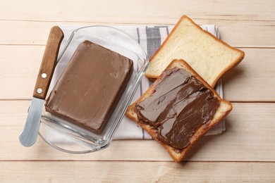 Photo of Block of tasty chocolate butter in keeper, slices of bread and knife on light wooden table, above view