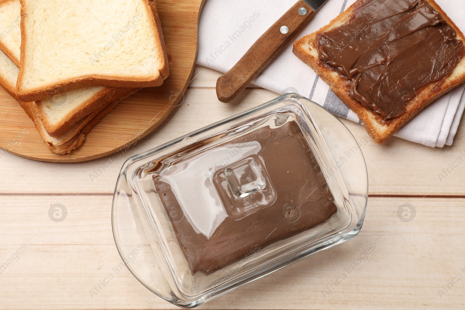Block of tasty chocolate butter in keeper and slices of bread on light wooden table, flat lay Photo of Block of tasty chocolate butter in keeper and slices of bread on light wooden table, flat lay