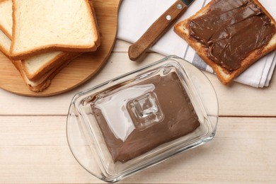 Photo of Block of tasty chocolate butter in keeper and slices of bread on light wooden table, flat lay