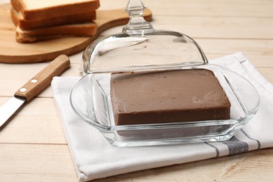 Photo of Block of tasty chocolate butter in glass keeper on light wooden table, closeup