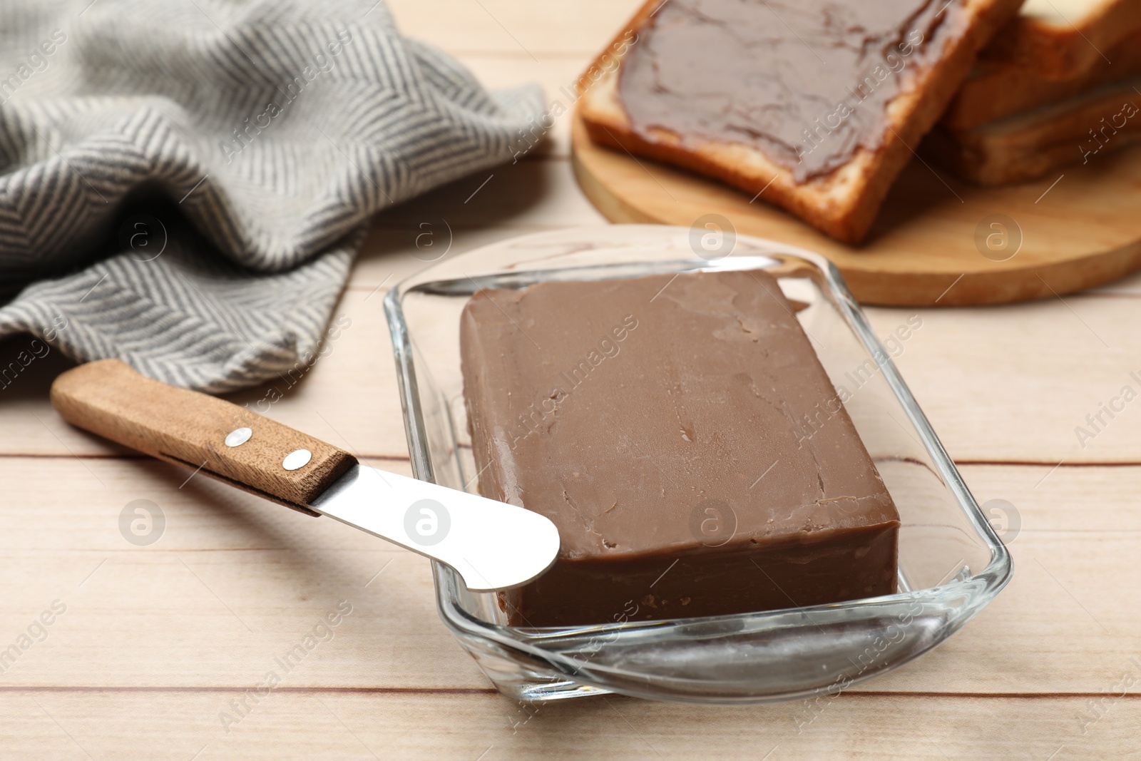 Block of tasty chocolate butter in glass keeper and knife on light wooden table, closeup Photo of Block of tasty chocolate butter in glass keeper and knife on light wooden table, closeup