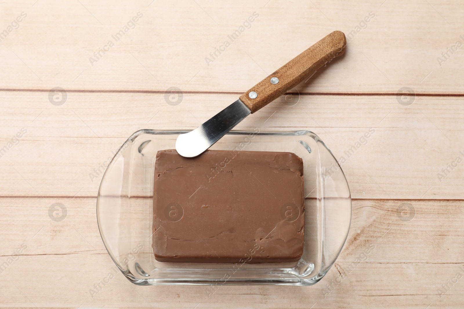 Block of tasty chocolate butter in glass keeper and knife on light wooden table, top view Photo of Block of tasty chocolate butter in glass keeper and knife on light wooden table, top view