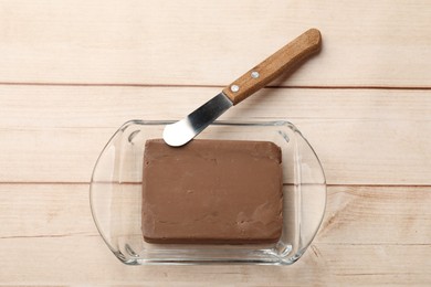 Photo of Block of tasty chocolate butter in glass keeper and knife on light wooden table, top view