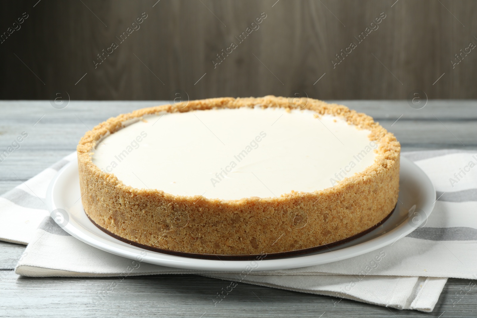 Photo of One tasty cheesecake on grey wooden table against brown background, closeup