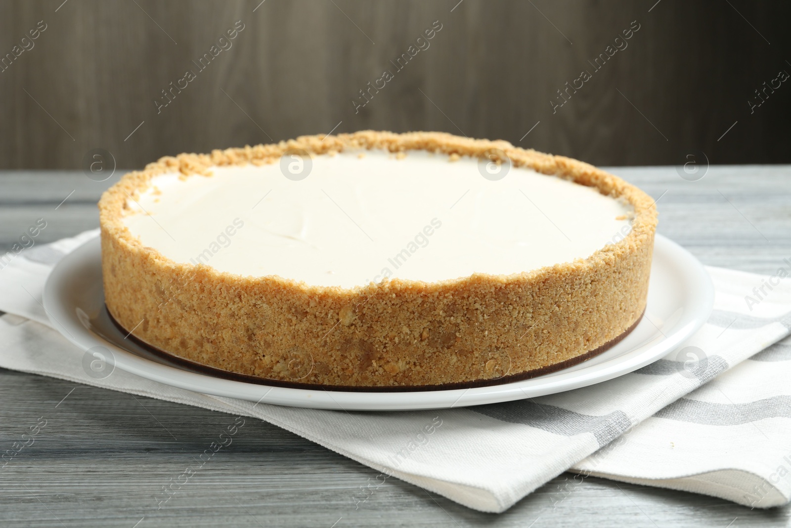 Photo of One tasty cheesecake on grey wooden table against brown background, closeup