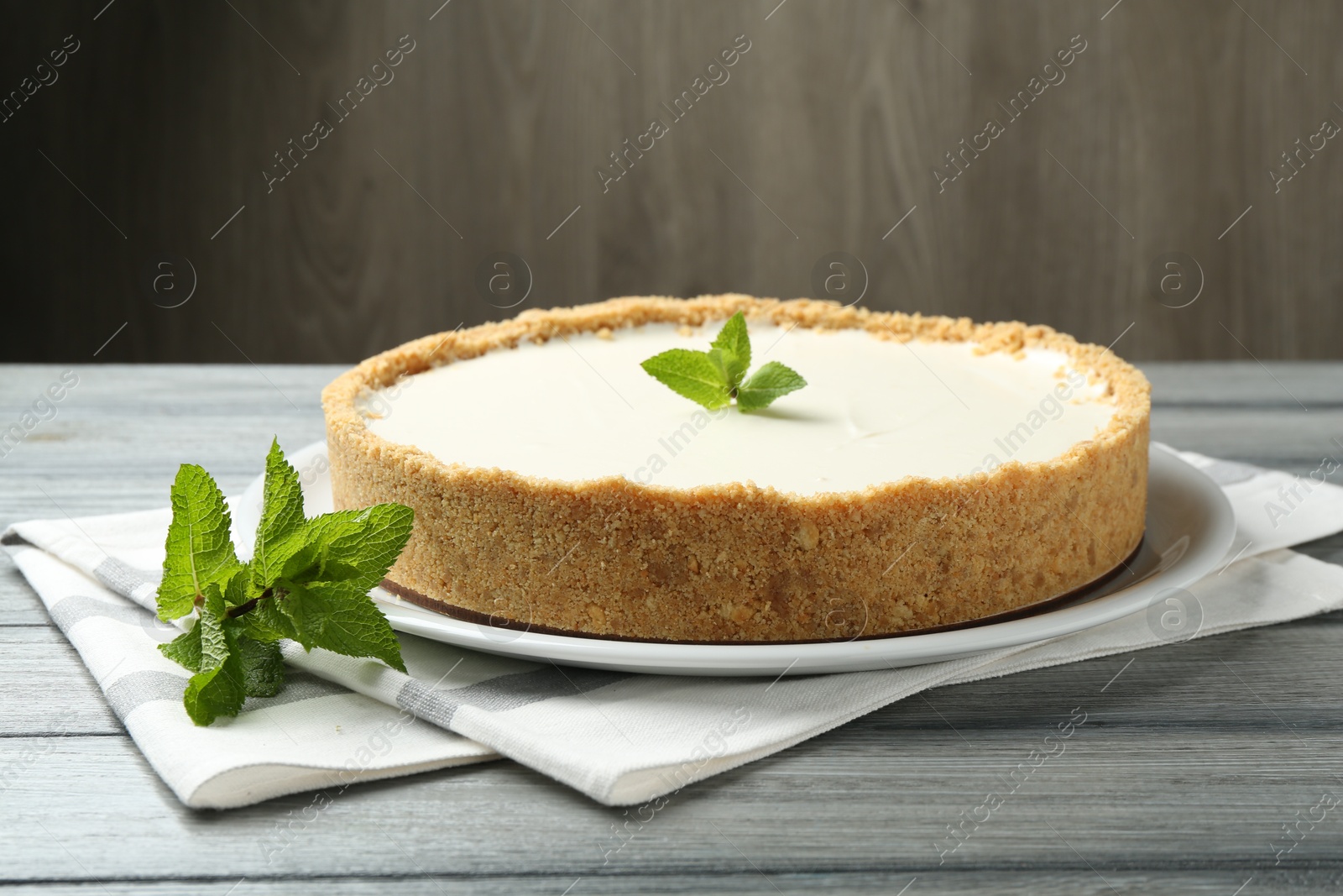 Photo of One tasty cheesecake with mint on grey table against wooden background, closeup