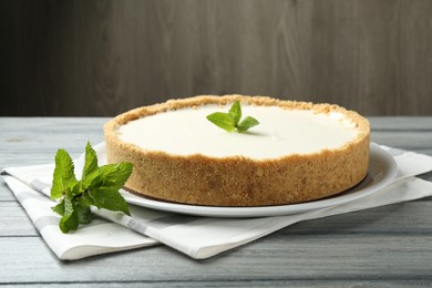 Photo of One tasty cheesecake with mint on grey table against wooden background, closeup