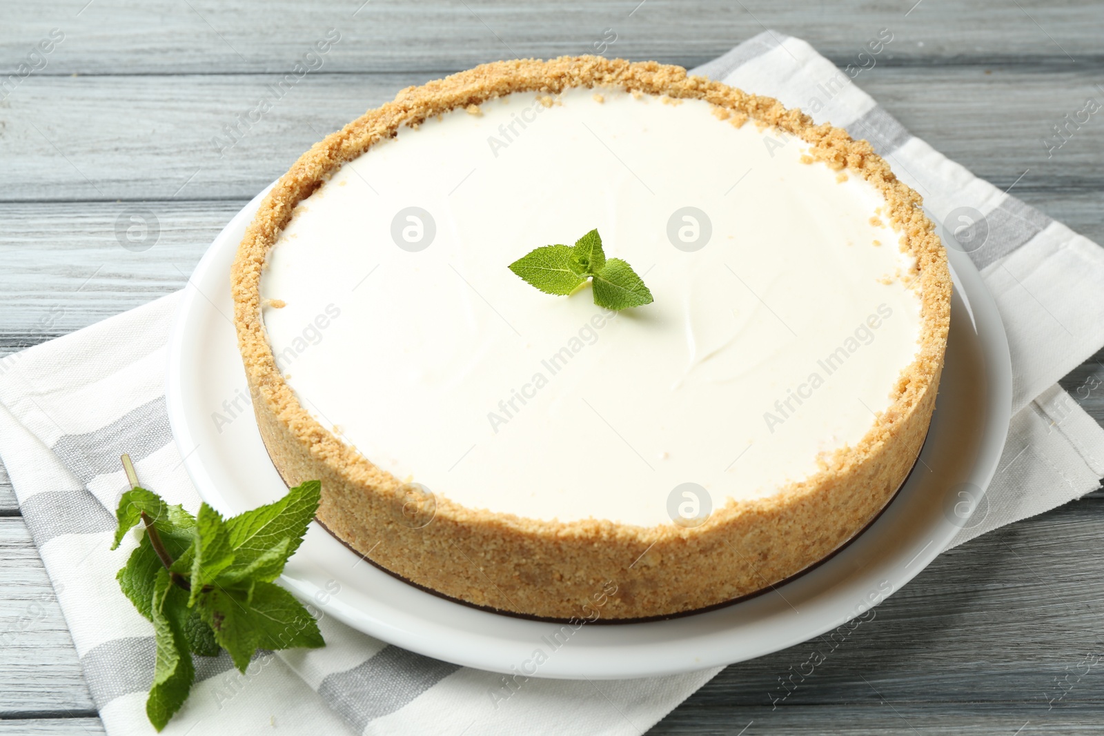 Photo of One tasty cheesecake with mint on grey wooden table, closeup