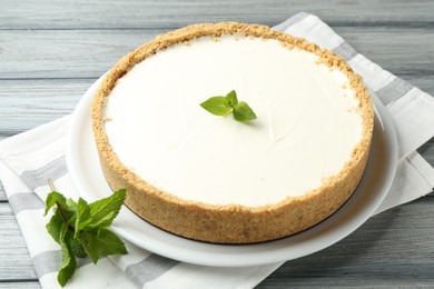Photo of One tasty cheesecake with mint on grey wooden table, closeup