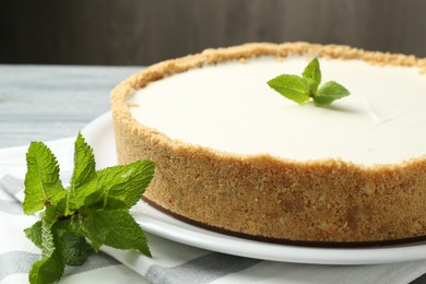Photo of One tasty cheesecake with mint on grey table against brown background, closeup