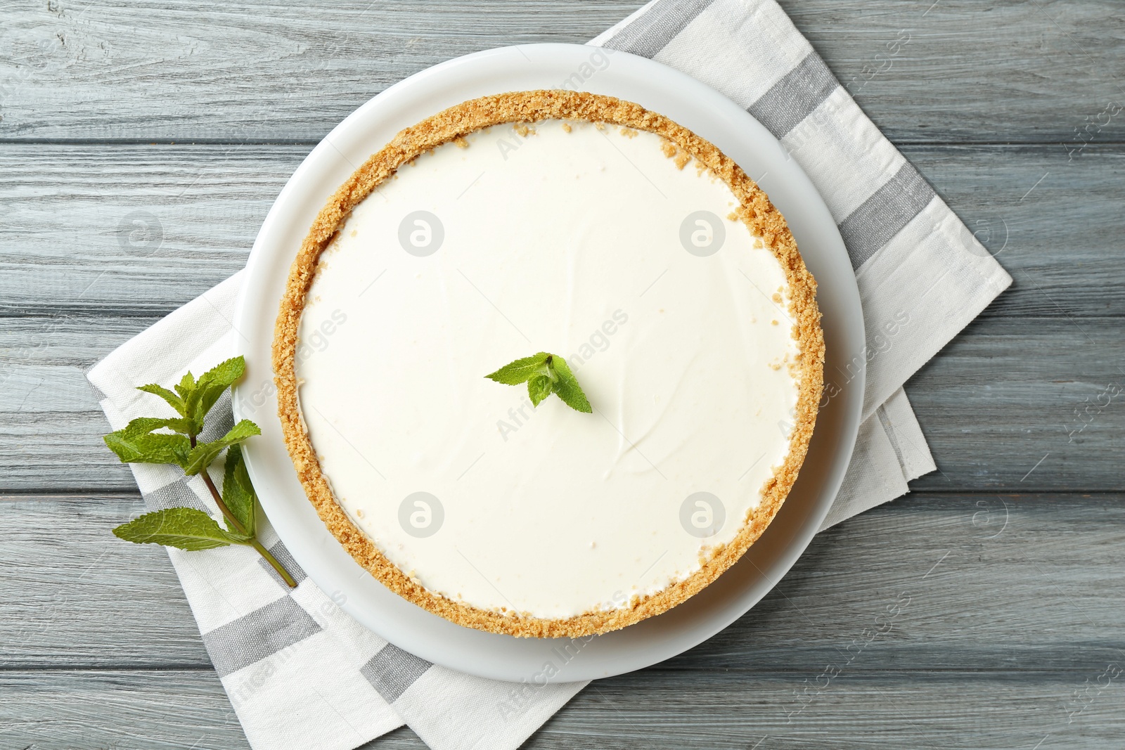 Photo of One tasty cheesecake with mint on grey wooden table, top view
