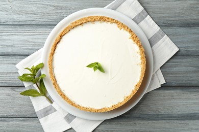 Photo of One tasty cheesecake with mint on grey wooden table, top view