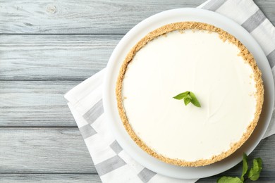 Photo of One tasty cheesecake with mint on grey wooden table, top view. Space for text