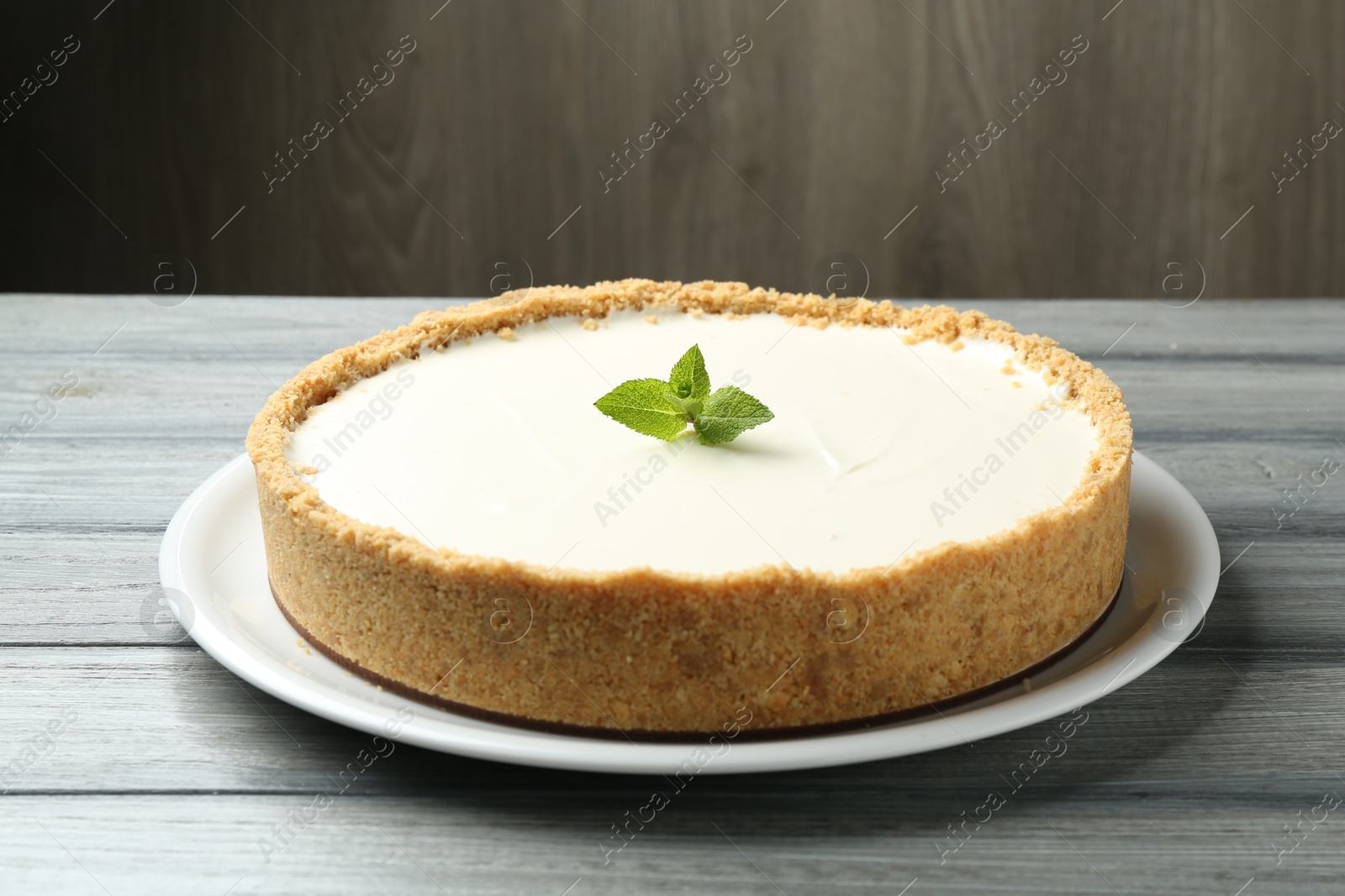Photo of One tasty cheesecake with mint on grey table against wooden background, closeup
