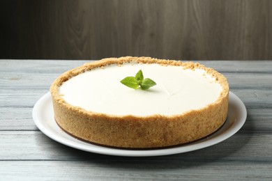 Photo of One tasty cheesecake with mint on grey table against wooden background, closeup