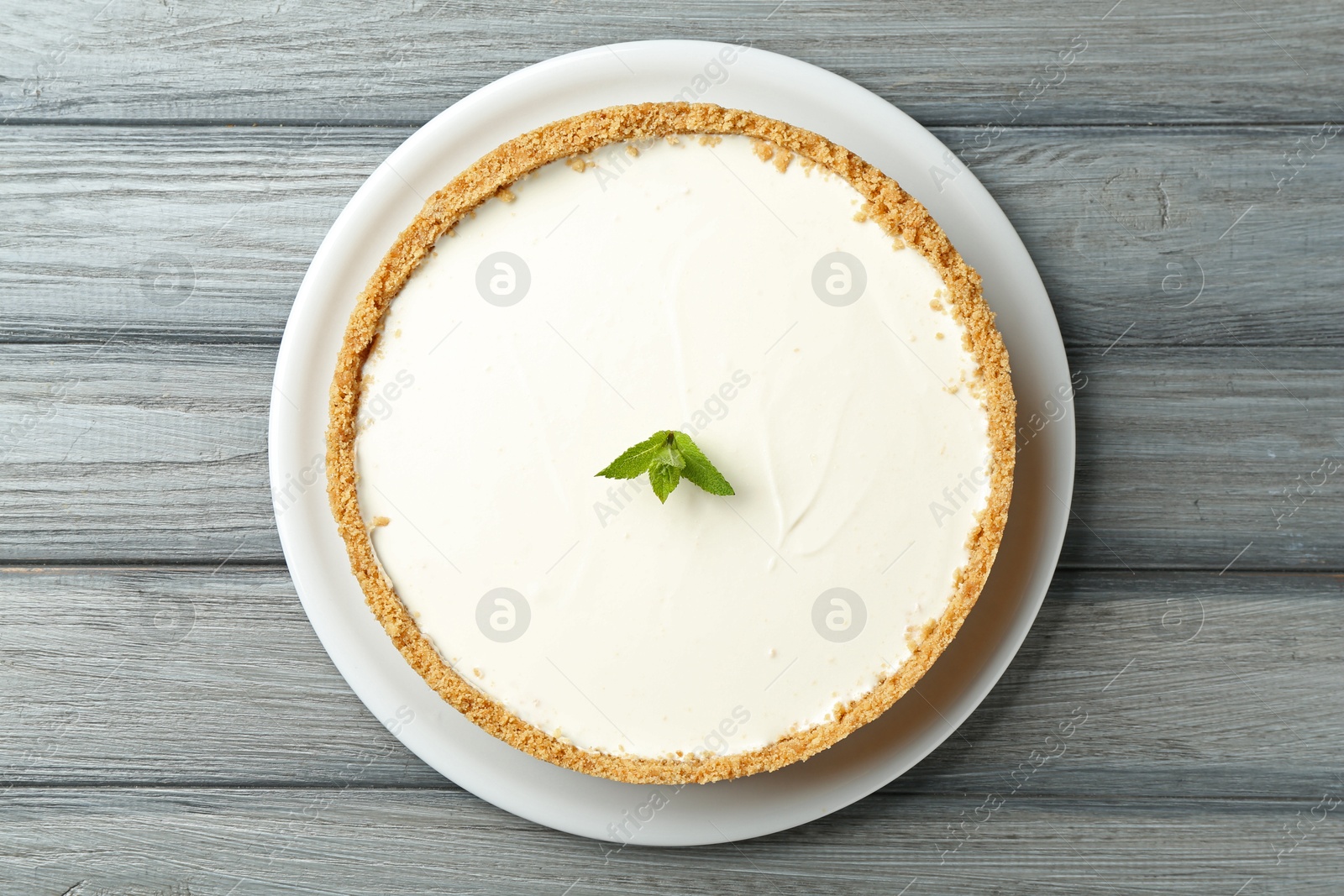 One tasty cheesecake with mint on grey wooden table, top view Photo of One tasty cheesecake with mint on grey wooden table, top view