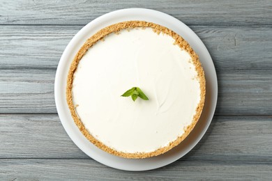 Photo of One tasty cheesecake with mint on grey wooden table, top view