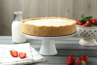Photo of One tasty cheesecake, strawberries and milk on grey table against wooden background, closeup