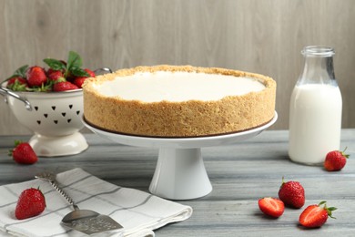 Photo of One tasty cheesecake, strawberries and milk on grey table against wooden background, closeup