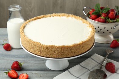 Photo of One tasty cheesecake, strawberries and milk on grey table against wooden background, closeup