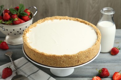 Photo of One tasty cheesecake, strawberries and milk on grey table against wooden background, closeup