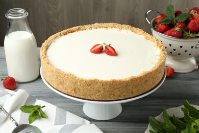 Photo of One tasty cheesecake, strawberries, mint and milk on grey table against wooden background, closeup