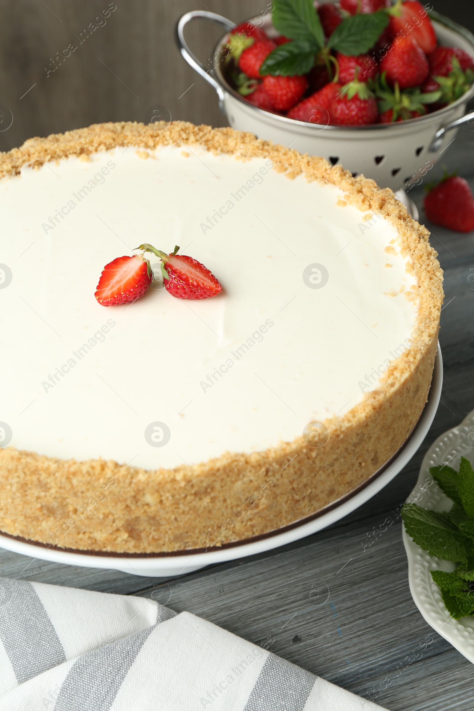 Photo of One tasty cheesecake, strawberries and mint on grey wooden table, closeup