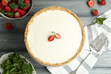 Photo of One tasty cheesecake, strawberries, mint and server on grey wooden table, flat lay