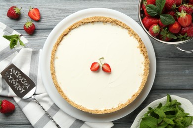 Photo of One tasty cheesecake, strawberries, mint and server on grey wooden table, flat lay
