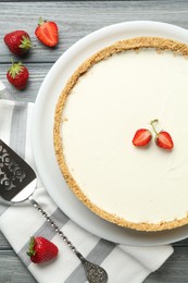 Photo of One tasty cheesecake, strawberries and server on grey wooden table, flat lay