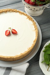 Photo of One tasty cheesecake, strawberries and mint on grey wooden table