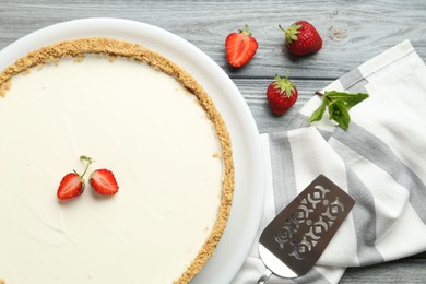 Photo of One tasty cheesecake, strawberries, mint and server on grey wooden table, flat lay