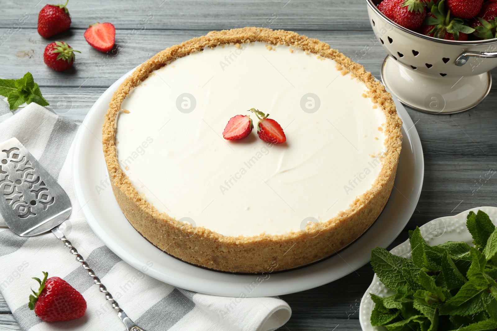 One tasty cheesecake, strawberries, mint and server on grey wooden table, closeup Photo of One tasty cheesecake, strawberries, mint and server on grey wooden table, closeup