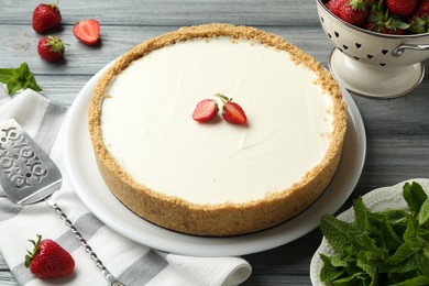 Photo of One tasty cheesecake, strawberries, mint and server on grey wooden table, closeup