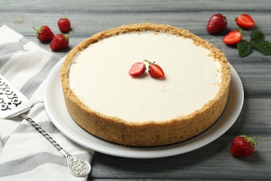 Photo of One tasty cheesecake, strawberries and server on grey wooden table, closeup