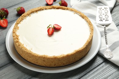 Photo of One tasty cheesecake, strawberries and server on grey wooden table, closeup